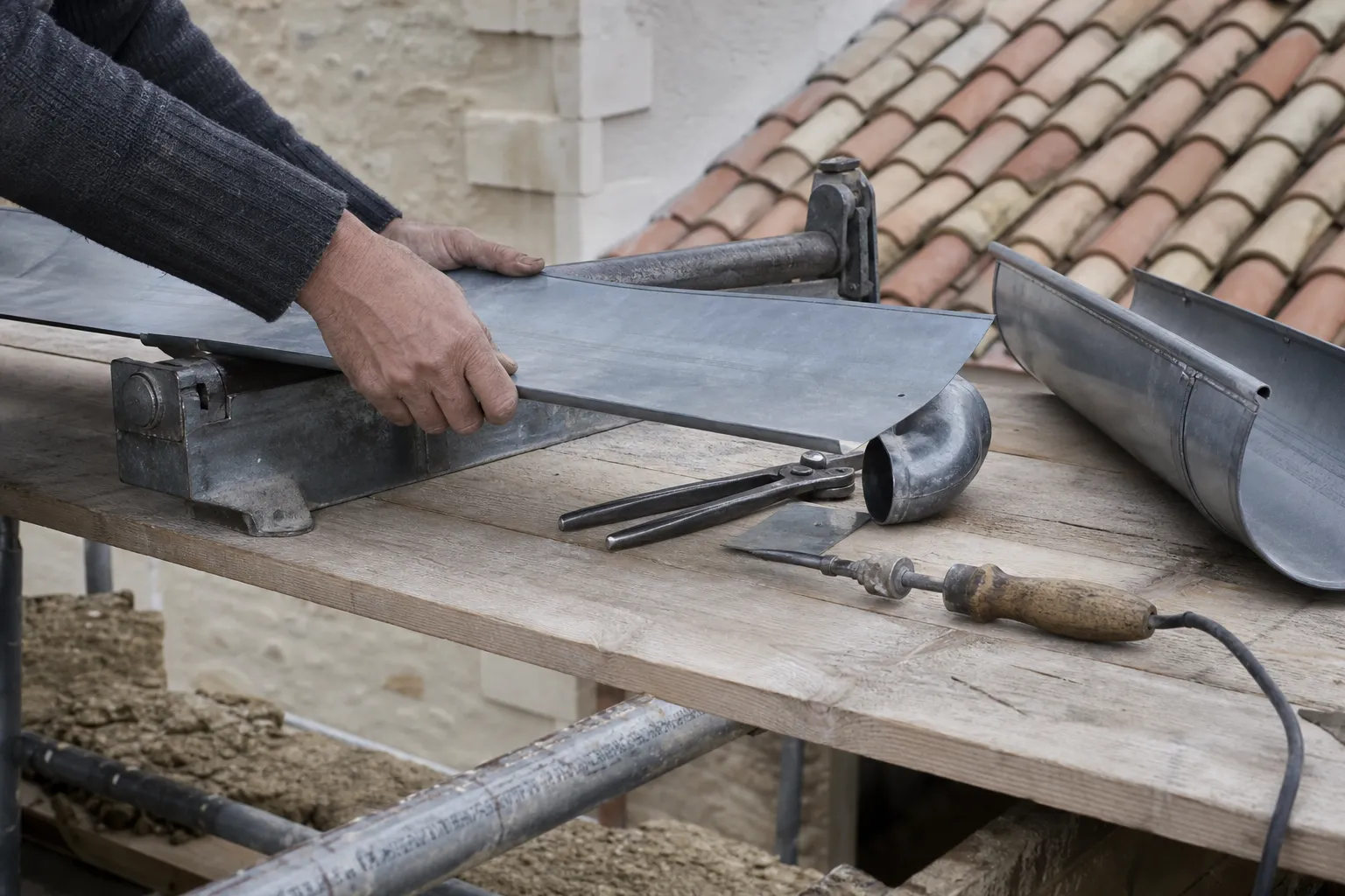 Feuille de zinc pliée à la plieuse à main, pinces à agrafer et fer à souder posés à côté