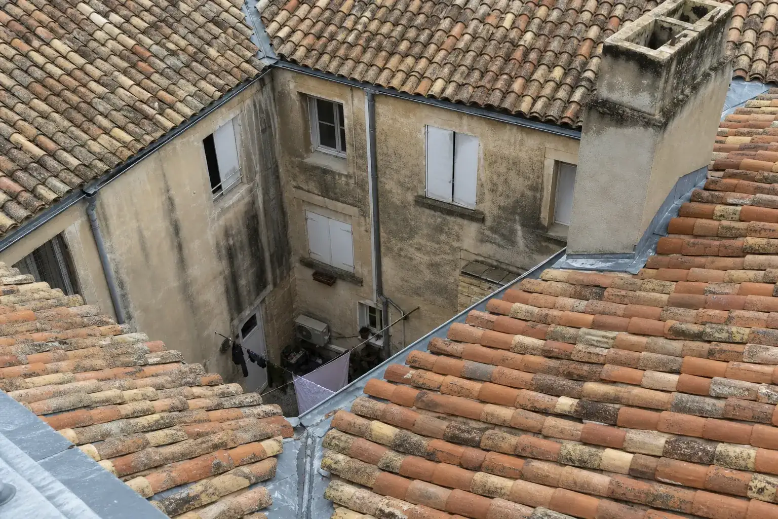 Cour intérieure étroite vue d’en haut, versants se rejoignant en noues, souche de cheminée enduite