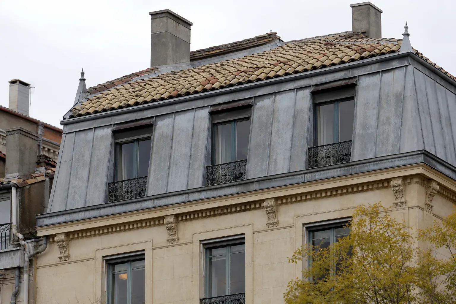 Étages hauts d’un immeuble de pierre, brisis en zinc oxydé et terrasson en tuile